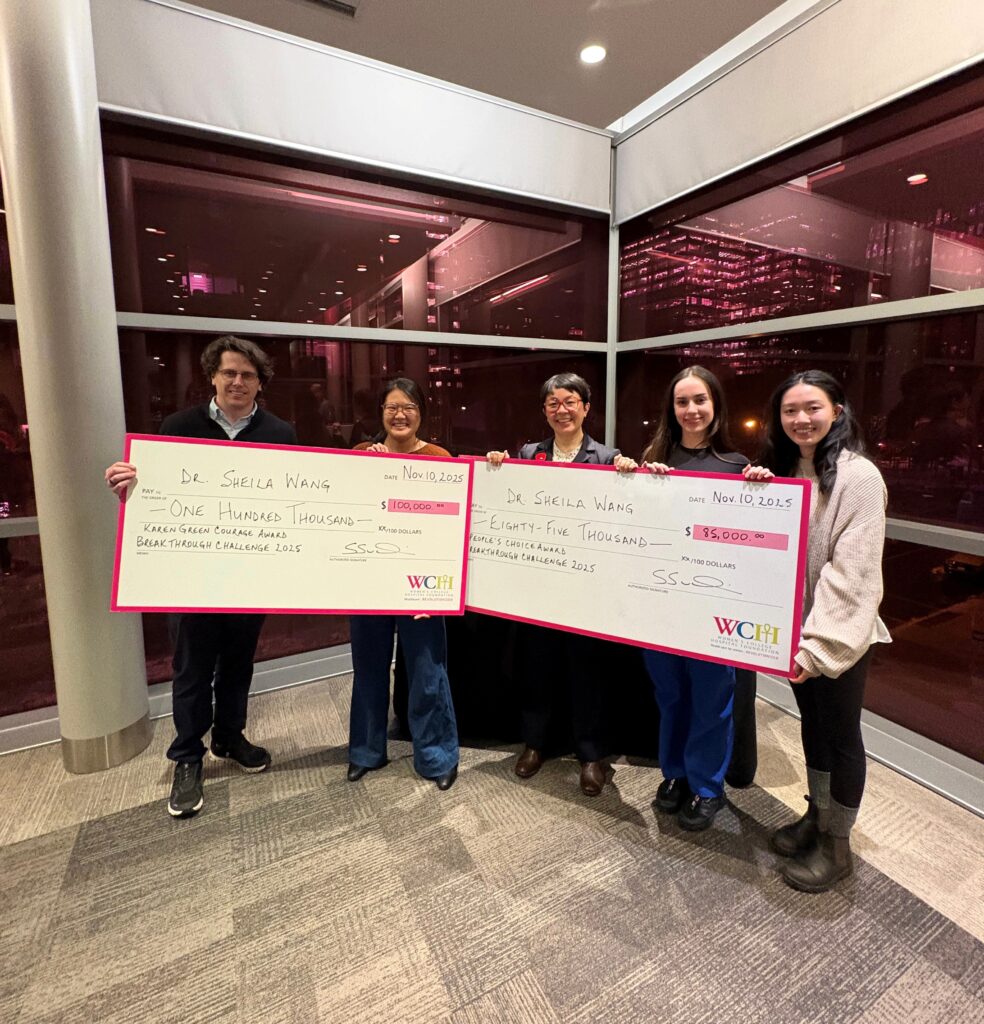 Six people hold two oversized cheques for $100,000 and $85,000, smiling indoors at night with city lights behind them.