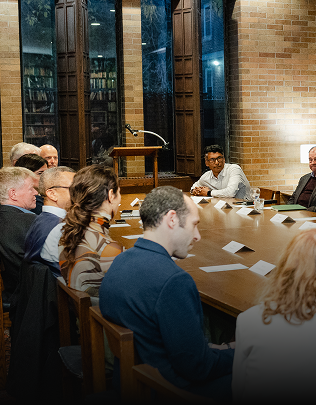 People sit around a table inside a building located on the Massey College campus
