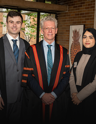 Principal of Massey College stands proudly with two students