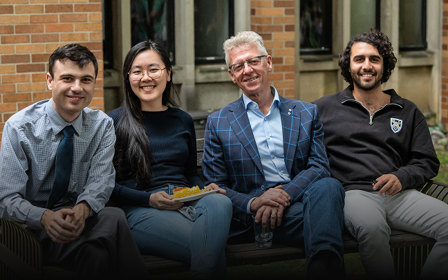 Members of the Quadrangle Society at Massey College sit, posing together and smiling for the camera